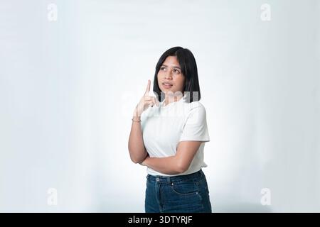Porträt einer jungen indonesischen Frau in einem weißen Hemd, die mit einem eureka-Ausdruck nach oben blickt. Konzept der Inspiration, Problemlösung und Kreativität. Stockfoto