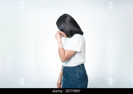 Seitenporträt einer jungen indonesischen Frau in einem weißen Hemd, die schüchtern nach unten blickt. Vorstellung von Bescheidenheit, Peinlichkeit oder geheim Lachen. Stockfoto