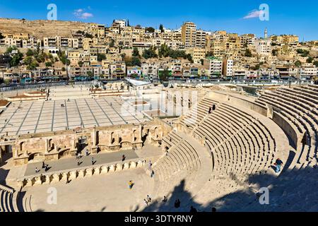 Besucher spazieren durch das römische Theater in Amman Jordan. Die antike Stätte ist von modernen Gebäuden und einem klaren blauen Himmel umgeben. Stockfoto