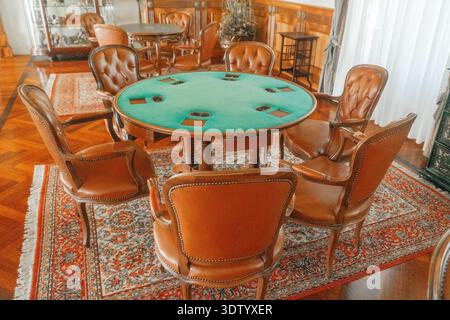 Spieltisch aus grünem Filz, umgeben von Lederstühlen im klassischen Interieur. Elegantes Holzdekor und Vintage-Atmosphäre. Stockfoto