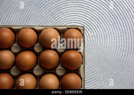 Ein sauberer, minimalistischer Blick von oben nach unten (flach) auf frische braune Hühnereier in einem grauen Karton. Der Karton wird auf einem modernen, silbernen, Stockfoto