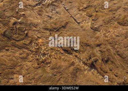 Eine Nahaufnahme des Wassers, das über eine felsige Oberfläche fließt, zeigt die natürliche Struktur und Muster des Bachbettes. Die Szene erfasst das dynamische m Stockfoto