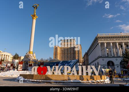 Aus der Vogelperspektive das Unabhängigkeitsdenkmal in Gold vor dem strahlend blauen Himmel, eingerahmt von dem ikonischen „I love Ukraine“-Schild in Kiew, Ukraine. Stockfoto
