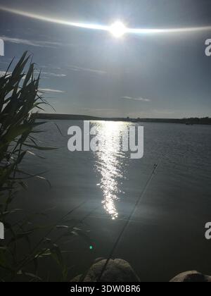 22 Grad Solar Halo über der Sonne über dem Calm Lake mit Angelrute – atmosphärisches Phänomen Stockfoto
