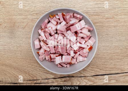 Gewürfelte geräucherte Speckstücke füllen eine graue Schüssel, von oben auf einer Holzoberfläche betrachtet Stockfoto
