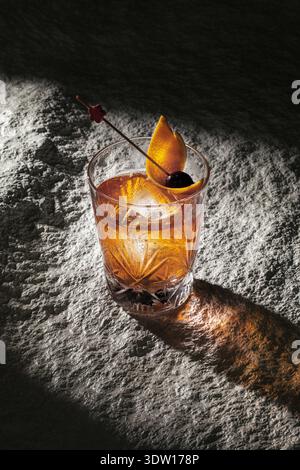 Klassischer Bernsteincocktail mit Orangenschale und Kirsche auf rauer Steinstruktur Stockfoto
