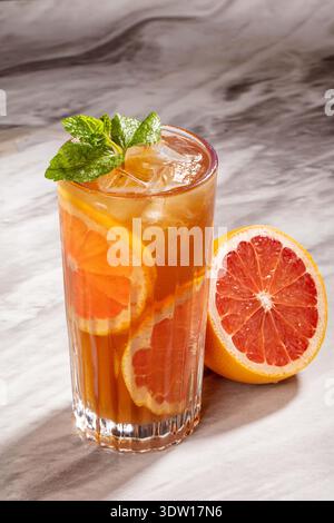 Erfrischender Grapefruit Iced Tea Cocktail mit frischen Minze- und Zitrusscheiben auf Marmoroberfläche Stockfoto