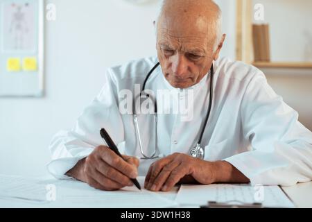 Älterer älterer männlicher Arzt oder Arzt trägt weiße Uniform mit Stethoskop arbeitet am Schreibtisch Gesundheitswesen in seinem Büro Arbeitsplatz. Medizin Stockfoto
