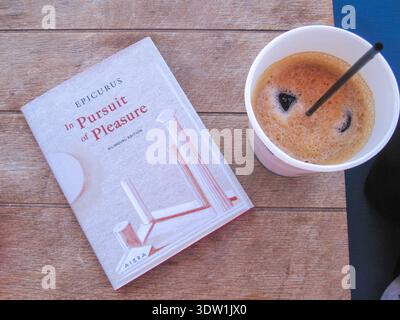 Kopie der zweisprachigen Ausgabe von Epicurus „in Pursuit of Pleasure“ neben einem Freddo-Espresso auf einem Holztisch, Griechenland Stockfoto