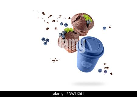Blue To Go Tasse heißer Kaffee und zwei Schokoladen Muffins mit Heidelbeeren und Krümeln fliegen isoliert auf weißem Hintergrund. Porzellan Reisebecher und Kubikku Stockfoto