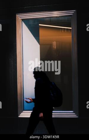 Der junge Mann läuft auf der Straße und hält sein Handy vor dem Fenster. Stockfoto
