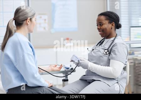 Junge Erwachsene Kaukasierin, deren Blutdruck von der Schwarzen Krankenschwester kontrolliert wurde Stockfoto