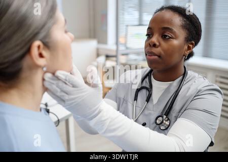 Junge Erwachsene Schwarze Frau Arzt untersucht Kaukasische Frau Patient in Klinik Stockfoto
