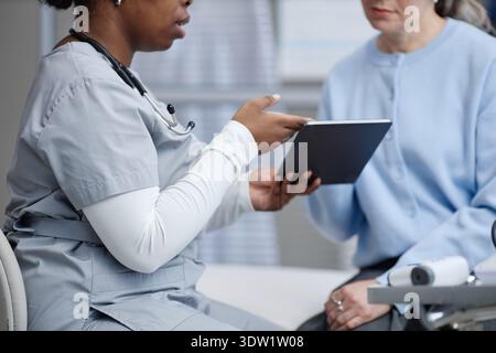 Schwarzer Frauenarzt mittleren Alters zeigt eine Tablette für eine weiße Frau mittleren Alters Stockfoto