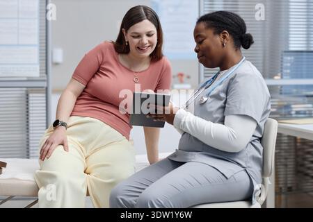 Weiße Frau Mittleren Alters Lächelt, Während Schwarze Krankenschwester Tablette Rezensiert Stockfoto