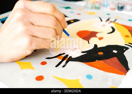 Eine Person malt während einer Bastelstunde am Wochenende ein buntes Motiv auf ein Stück Papier. Pinsel und Farben sind im Hintergrund sichtbar. Stockfoto