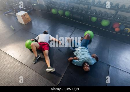 Zwei afrikanische Männer, die Trainingskleidung tragen und auf Stoffmatten liegen, mit grünen Medizinbällen Stockfoto