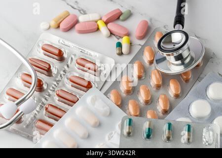 Blisterpackungen mit Arzneimitteln in Form von Kapseln und Tabletten und Stethoskopkopf auf Marmorhintergrund. Bunte Pillen. Pharmazeutische Hilfe und h Stockfoto