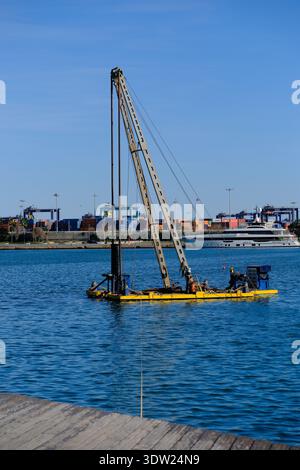 20. Feb 2026 - Valencia, Spanien - Ein Boot für den Bau eines Yachthafens, das Pfahlbauten in die Bucht wirft, um einen Yachthafen oder einen Dock zu bauen Stockfoto