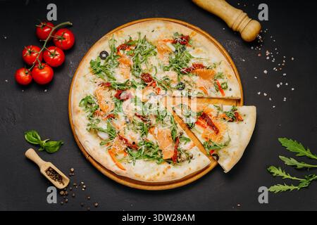Gourmet-Pizza mit Lachs-Rucola-Käse und sonnengetrockneten Tomaten auf Holzbrett Stockfoto