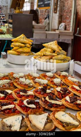 Eine Auswahl an frisch gebackenen herzhaften Tartlets mit Tomaten, Oliven und Käse sowie Stapel von goldbraunen Phyllo-Teigdreiecken auf einem Markt in Cape Stockfoto