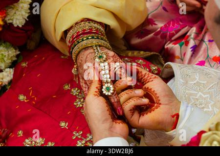 Nahaufnahme eines hinduistischen Bräutigams, der während einer traditionellen indischen Hochzeitszeremonie mit goldjude einen Diamantring am Henna-geschmückten Finger der Braut platziert Stockfoto
