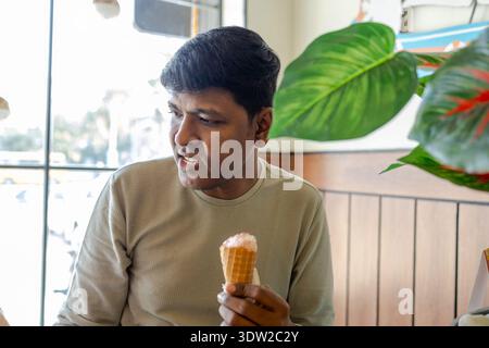 Der Mann sitzt in einem Café und hält eine Eiskugel und genießt seine Leckereien am Nachmittag. Stockfoto