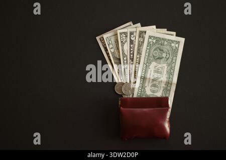 US-Dollar-Banknoten und -Münzen neben brauner Ledergeldbörse auf schwarzem Hintergrund Stockfoto