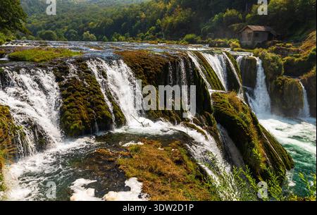 Una River Wasserfälle zeigen natürliche Schönheit und fließendes Wasser schaffen eine ruhige Landschaft mit einem kleinen Haus auf dem Hügel, Bosnien und Herzegowina. Stockfoto
