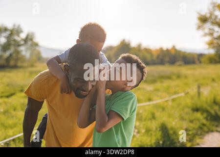Ein alleinerziehender Vater teilt mit seinen Söhnen freudige Momente in einem Park während des Sonnenuntergangs. Sie spielen und binden sich in der Natur. Stockfoto