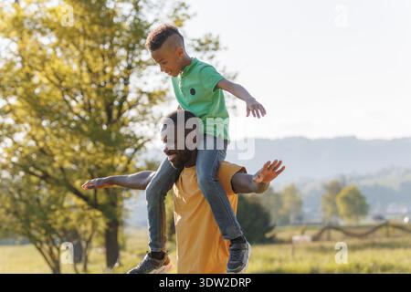 Der afroamerikanische Vater teilt mit seinen Kindern während des Sonnenuntergangs lustige Momente in der Natur und fördert Familienbande und Freude. Stockfoto