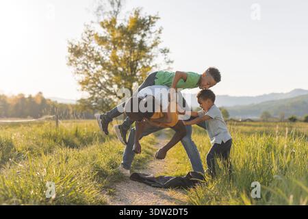 Vater genießt die Zeit mit seinen Kindern im Freien und teilt spielerische Momente in der Natur, während die Sonne hinter ihnen untergeht. Stockfoto