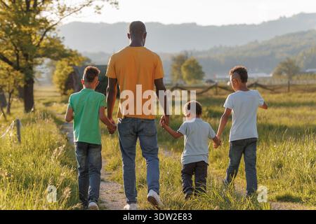 Alleinerziehender Vater genießt die Zeit mit seinen Kindern im Freien in einer grasbewachsenen Gegend, während die Sonne hinter ihnen untergeht. Sie teilen Momente der Freude und des Lachens. Stockfoto
