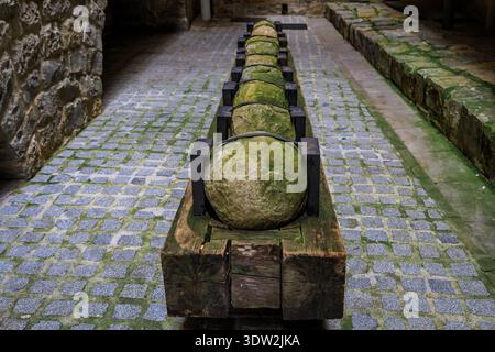Reihe großer Steinkanonenkugeln, die in einer hölzernen Wiege auf einer Kopfsteinpflasterstraße in der Altstadt oder im Casco Viejo in Pamplona, Spanien, aufbewahrt und gesichert wurden Stockfoto