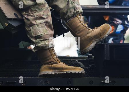 Nahaufnahme eines Soldaten in Tarnhosen und taktischen Wüstenstiefeln, der während einer Militärmission auf einem gepanzerten Fahrzeug sitzt. Stockfoto