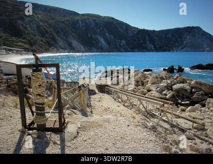 Bootsrutsche mit Holzschienen am Petani Beach, Kefalonia, Griechenland. Atemberaubendes türkisfarbenes Ionisches Meer und zerklüftete Kalksteinklippen in der Sonne. Stockfoto