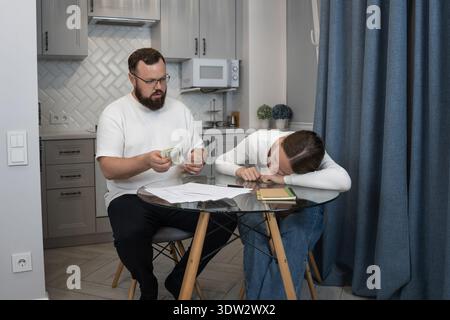 Ein Paar hat finanzielle Schwierigkeiten in der Küche, der Mann zählt Geld und die Frau sieht erschöpft aus, was Stress, Schulden und Budget symbolisiert Stockfoto