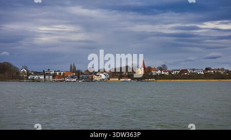 Blick vom Strelasund auf das Panorama der Altefähr auf Rügen mit der Nikolaikirche unter einem dramatischen, bewölkten Himmel Stockfoto