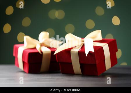 Schöne Samtgeschenkdosen auf schwarzem Holztisch vor dunkelgrünem Hintergrund mit verschwommenen Lichtern, Nahaufnahme. Bokeh-Effekt Stockfoto