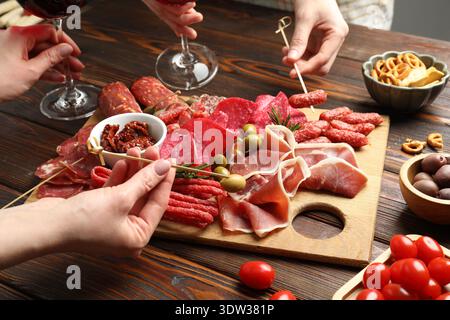 Die Leute essen leckere Snacks von der Wurstplatte am Holztisch, Nahaufnahme Stockfoto