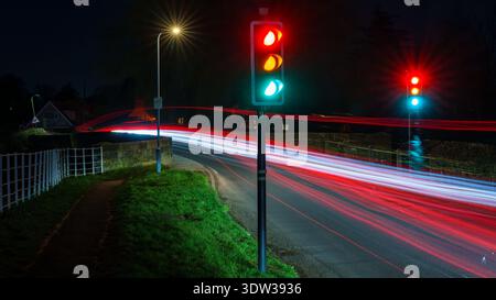 Nächtliche Verkehrsszene mit lange belichteten Lichtspuren an einer Straßenkreuzung, beleuchteten Ampeln in Rot und Grün, Straßenlaternen-Leuchten, nassem Roa Stockfoto