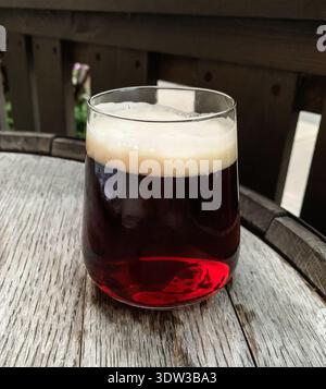Nahaufnahme eines Glases dunkles Bier mit cremigem Schaumkopf auf einem rustikalen Holzfasstisch. Bild von Brauerei und Pub-Konzept. Stockfoto