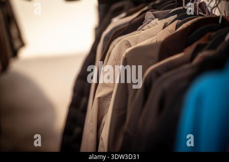 Aus nächster Nähe sehen Sie Second Hand-Mäntel an Kleiderbügeln in einem Second-Hand-Geschäft, in dem die Wiederverwendung und der Wiederverkauf von Kleidung, nachhaltiges Einkaufen und die Kreislaufwirtschaft AS hervorgehoben werden Stockfoto