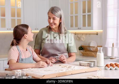 Lächelnde Großmutter und ihre Enkelin kochen zusammen am Tisch in der Küche Stockfoto