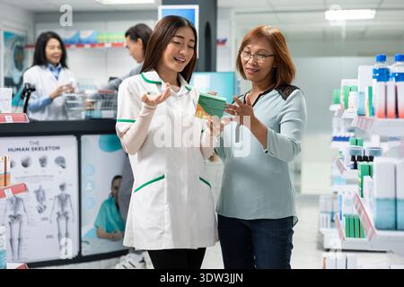 Freundlicher Apotheker bietet medizinische Beratung für Frau mittleren Alters, erklärt Rezeptdetails, Medikamentenflaschenverbrauch, Nebenwirkungen und Wellness-Optionen in der lokalen Apotheke. Stockfoto