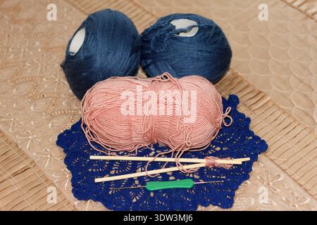 Stillleben der Herstellung von Vorräten zum Stricken von Häkeln. Rosafarbene dunkelblaue Garnbällchen ruhen auf einem blauen Deckchen beigen Stoff. Holzstricknadeln ein grünes cro Stockfoto