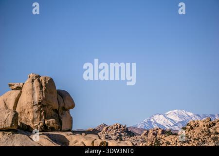 Ein großer Felsen liegt auf einem felsigen Hügel inmitten einer Bergkette. Der Himmel ist klar und blau, und die Berggipfel sind mit Schnee bedeckt. Die sc Stockfoto