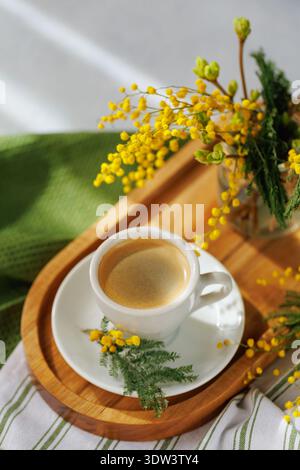 Frisch gebrühter Kaffee mit Mimosa-Blüten auf einem Tablett Stockfoto