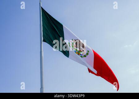 Nationalflagge von Mexiko mit dem Wappen des Adlers, das im Wind vor einem klaren blauen Himmel winkt. Stockfoto