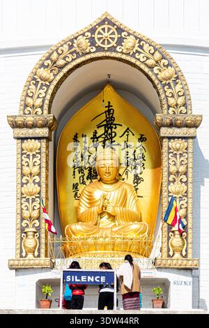 Eine heitere goldene Buddha-Statue in einer Stupa in Nepal, mit Besuchern, die Stille beobachten. Stockfoto